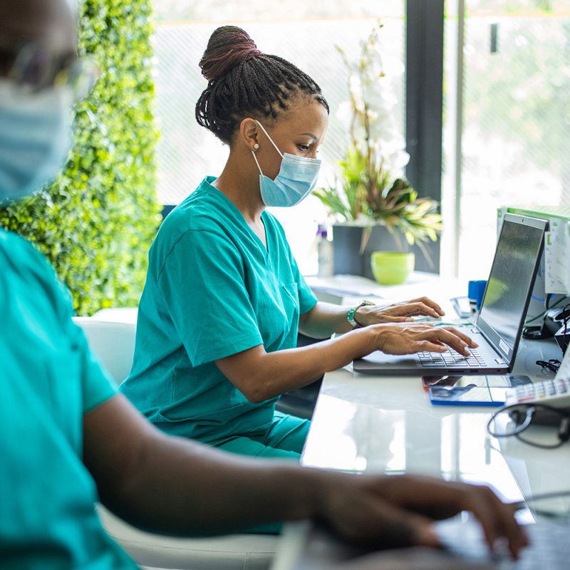 Nurse with protective facemask workin on laptop