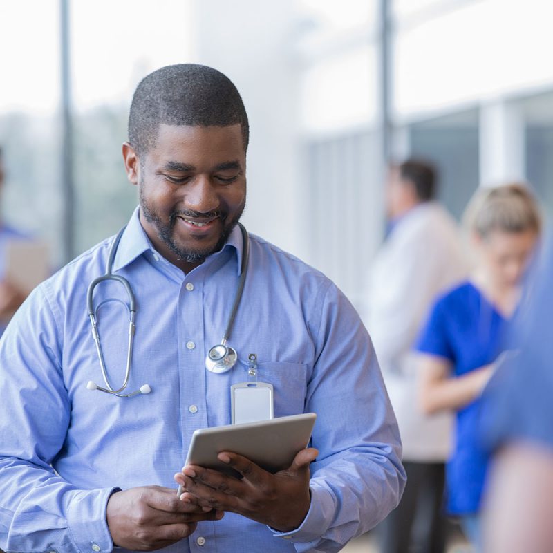 Mature hospital administrator or doctor looks at electronic patient file on digital tablet while working in crowded hospital