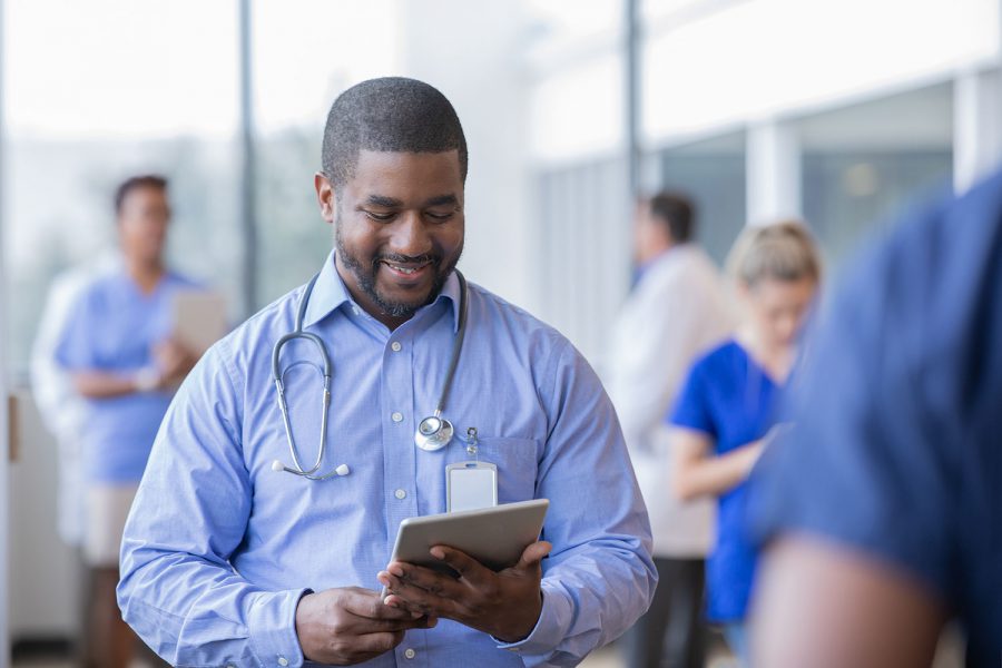 Mature hospital administrator or doctor looks at electronic patient file on digital tablet while working in crowded hospital